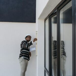 Architect with hard hat inspecting glass doors in a modern building outdoors.