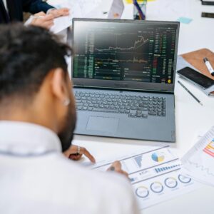 Business professionals analyzing stock charts and graphs on a laptop in an office setting.